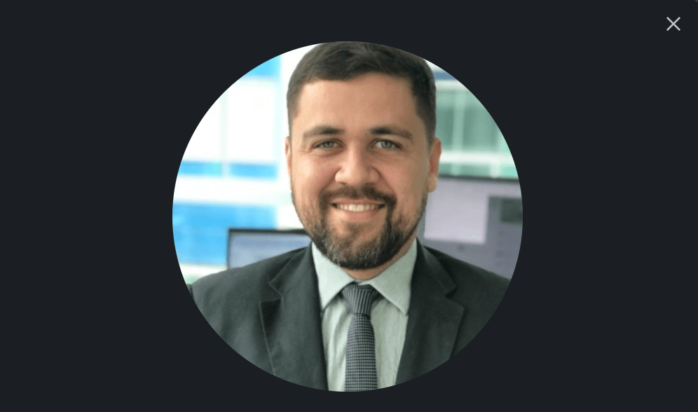 Smiling man with a beard wearing a professional suit and tie in an office setting.