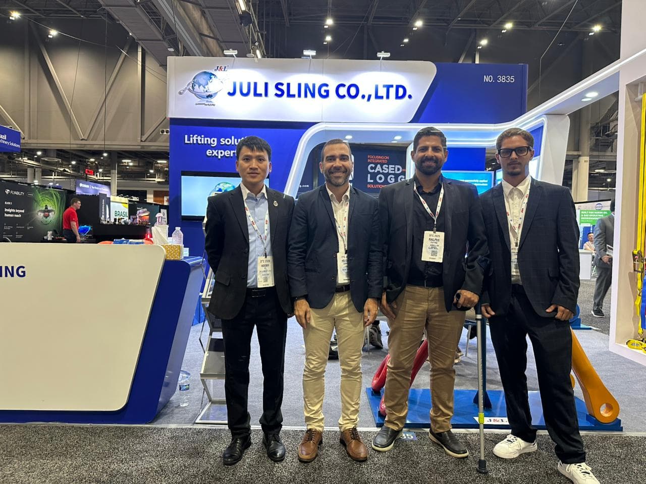 Four men in professional attire stand before a Juli Sling Co. trade show booth.