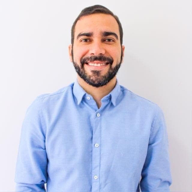 Smiling man with a dark beard and short hair wearing a light blue button-down shirt.