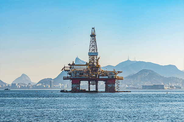 Offshore oil rig in the ocean with Rio de Janeiro's mountains and city skyline in the background.
