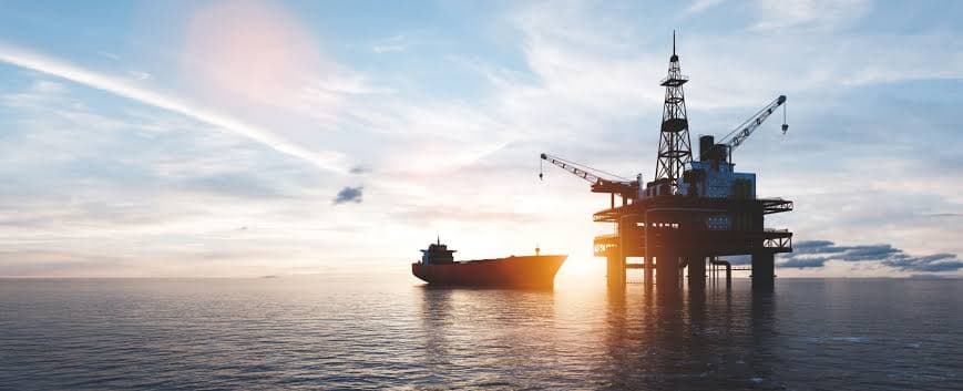 Silhouetted offshore oil rig and tanker ship on the ocean during a golden sunset.